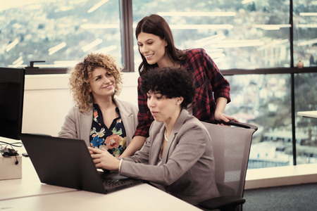 Group of young female software developers using laptop computer while writing programming code at modern creative startup officeの写真素材