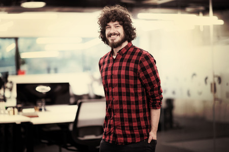 Portrait of young smiling successful male software developer standing at modern startup officeの写真素材