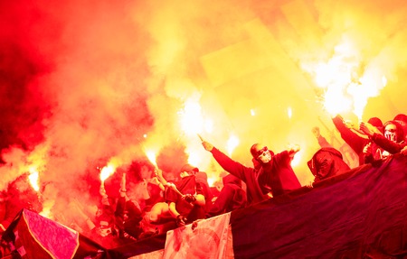football hooligans with mask holding torches in fire while supporting their favorite team during a match at stadiumのeditorial素材