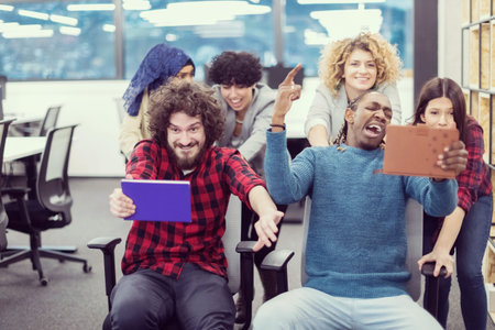multiethnics startup business team of software developers having fun while racing on office chairs,excited diverse employees laughing enjoying funny activity at work break, creative friendly workers playing game togetherの写真素材