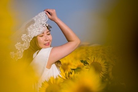 Young happy Asian woman in wedding dress having fun and relax on Sunflower fieldの写真素材