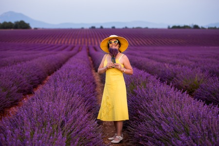 beautiful young asian woman in yellow dress and hat relaxing and having fun on purple flower lavender fieldの写真素材