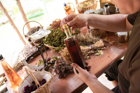 Tincture or potion bottle in hand of herbalist  bunch of dry healthy herbs in  alternative medicineの写真素材