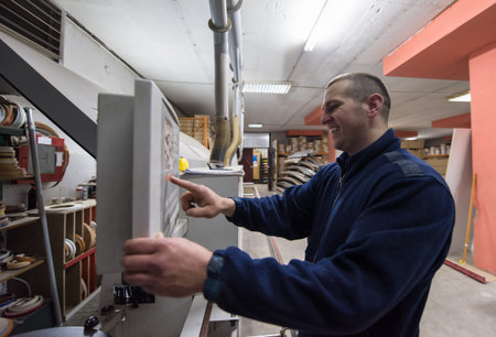 young carpenter calculating and programming a cnc wood working machine in workshop. wood worker...