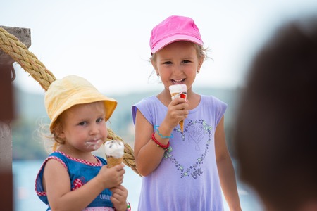 adorable little girls eating ice cream on beach by the sea during Summer vacationの写真素材
