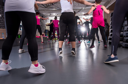 A group of young healthy sporty women working out with instructor doing aerobics exercises in a...
