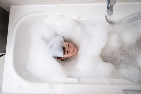 Top view of little girl playing with soap foam in bath