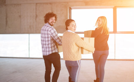 happy young casual business team carrying cardboard boxes with sunlight through the windows during...