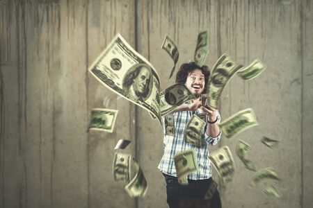 business, people and finances concept  Happy young businessman throwing US dollar banknotes and enjoying while making the rain of money in new startup officeの写真素材