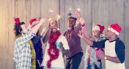 multiethnic group of young happy casual business people dancing with sparklers and having fun while celebrating new year eve in front of concrete wall at new startup officeの写真素材
