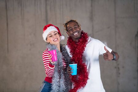 young casual multiethnic business couple having fun while celebrating new year party in unfinished startup office with a gray wall behind themの写真素材