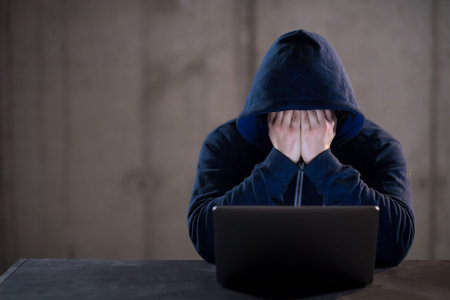 Young talented hacker using laptop computer while working in dark office with concrete wall in the...