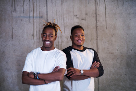 portrait of two young african american smiling casual businessmen standing in front of a concrete wall at new startup officeの写真素材