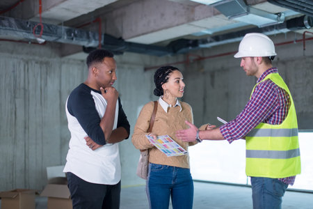 architect engineer using tablet computer while showing house design plans to a young multiethnic...