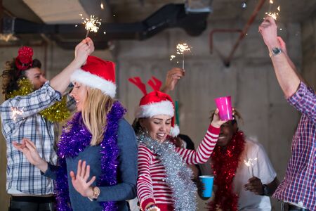 multiethnic group of young happy casual business people dancing with sparklers and having fun while celebrating new year eve in front of concrete wall at new startup officeの写真素材