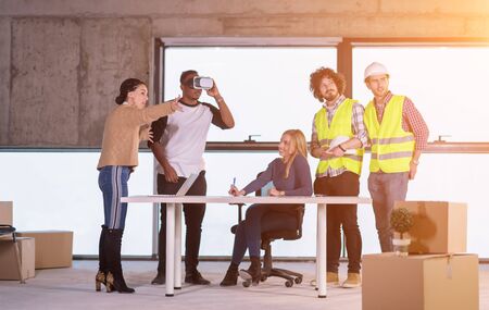 young multiethnic business team checking documents and business workflow on construction site using the virtual reality headset and laptop computer with sunlight through the windows during moving in at new startup officeの写真素材
