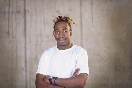 portrait of young african american smiling casual businessman standing in front of a concrete wall...