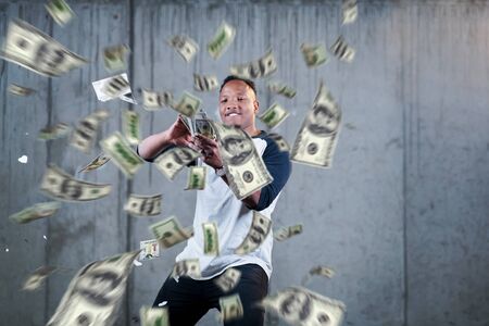 business, people and finances concept  Happy young african american businessman throwing US dollar banknotes and enjoying while making the rain of money in new startup officeの写真素材