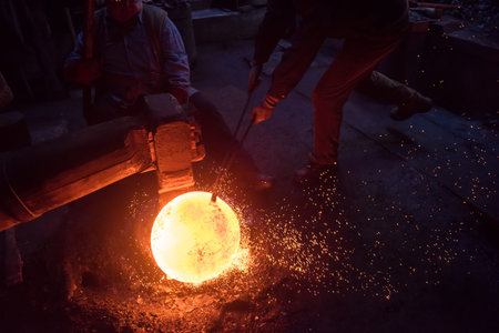 two real brutal traditional blacksmith workers working together with a red hot iron using mechanical...