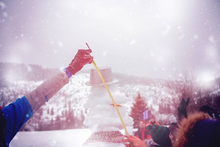 group of young happy business people after a competition measuring the height of finished snowman while enjoying snowy winter day with snowflakes around them during a team building in the mountain forestの写真素材