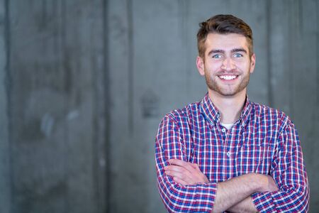 portrait of young successful smiling casual businessman standing in front of a concrete wall at new startup officeの写真素材