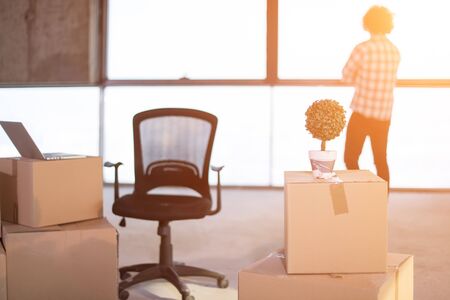 rear view of young casual businessman standing with crossed arms on construction site and sunlight through the windows during moving in at new startup officeの写真素材