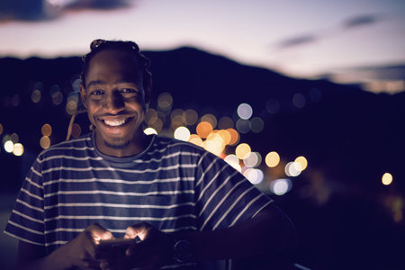 Young manl on urban city  street at night texting on smartphone with bokeh and neon city lights in...