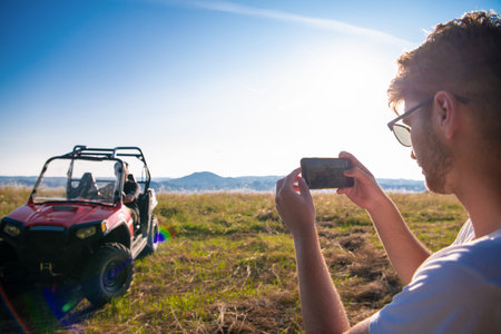 young man enjoying beautiful sunny day taking a picture of his friend while driving a off road buggy...