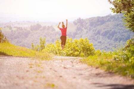 young happy woman enjoying in a healthy lifestyle while jogging on a country road through the beautiful sunny forest, exercise and fitness conceptの写真素材