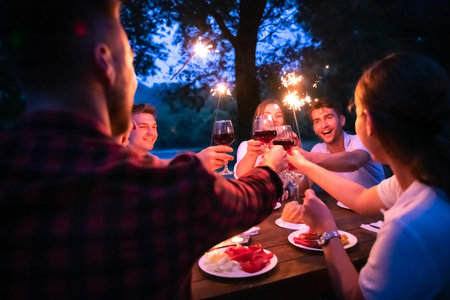 group of happy friends celebrating holiday vacation using sprinklers and drinking red wine while...