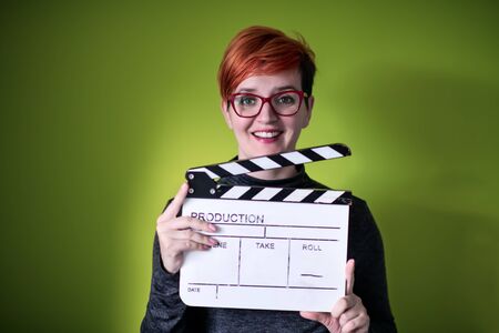 redhead woman holding movie clapper isolated against green background cinema concept in studioの写真素材