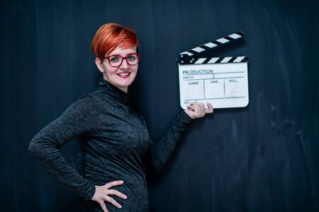 redhead woman on black chalkboard holding movie clapper cinema conceptの写真素材