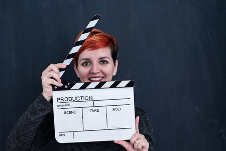 redhead woman on black chalkboard holding movie clapper cinema concept