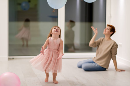 happy family spending time together young redhead mother and cute little daughter having fun while playing with balloons near the window on beautiful evening at homeの写真素材