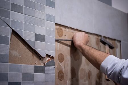 professional worker remove demolish old tiles in a bathroom with hammer and chiselの写真素材
