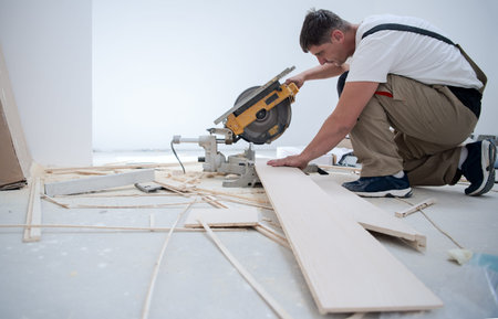 professional worker cutting plank with electrical circular saw during installation a new laminated...