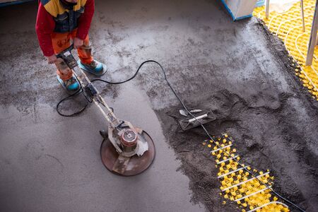 Laborer performing and polishing sand and cement screed floor on the construction site of a new two-level apartment. Sand and cement floor screedの写真素材