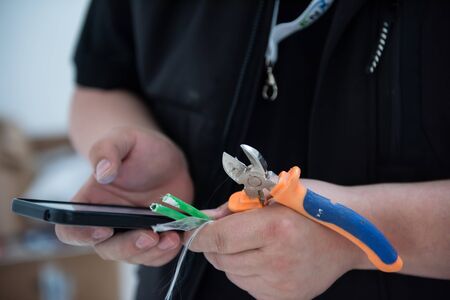 electrical engineer with wire and pliers in his hand using mobile phone while working on electrical installations in a new apartmentの写真素材