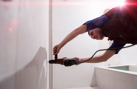 young professional construction worker drilling holes in the bathroom wall for installing bathroom accessoriesの写真素材