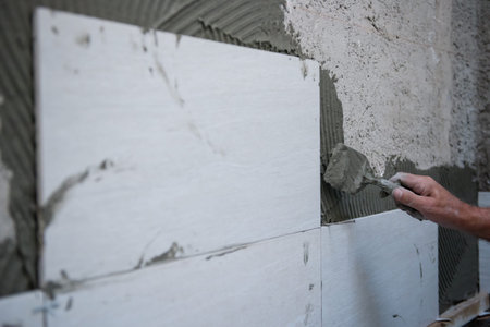 experienced senior construction worker installing big ceramic tiles on interior concrete walls