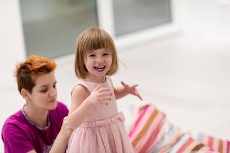 family having fun on beutiful evening at home young mother helping cute little daughter while putting on a pink dress for dancing at homeの写真素材