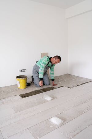 skilled worker installing the ceramic wood effect tiles on the floor Worker making laminate flooring on the construction site of the new apartmentの写真素材
