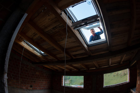 construction worker installing environmentally friendly and energy efficient roof window. Room under...