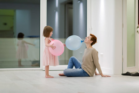happy family spending time together young redhead mother and cute little daughter having fun while playing with balloons near the window on beautiful evening at homeの写真素材
