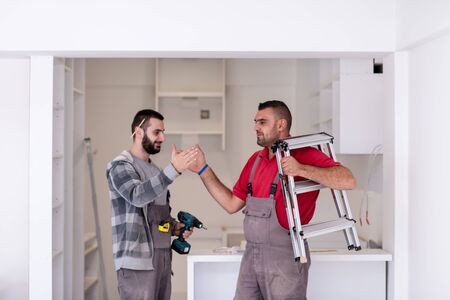 two professional workers giving high five to each other during installation a new stylish modern kitchen furnitureの写真素材