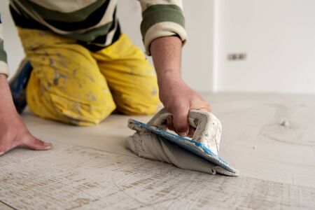 Grouting ceramic tiles. Tilers filling the space between ceramic wood effect tiles using a rubber trowel on the floor in new modern apartmentの写真素材