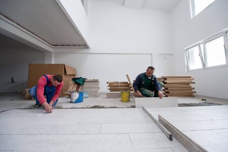 skilled workers installing the ceramic wood effect tiles on the floor Workers making laminate flooring on the construction site of the new apartmentの写真素材