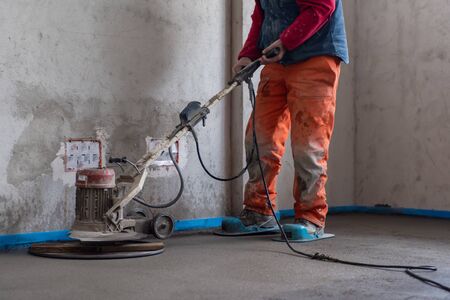 Laborer performing and polishing sand and cement screed floor on the construction site of a new two-level apartment. Sand and cement floor screedの写真素材