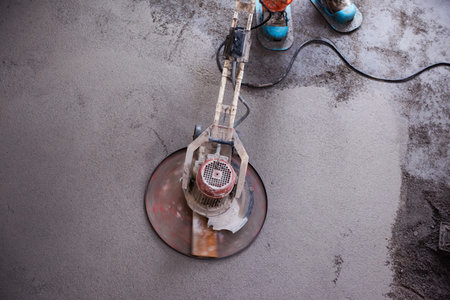 Laborer performing and polishing sand and cement screed floor on the construction site of a new...