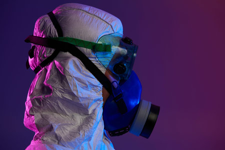 Coronavirus covid-19  pandemic. Doctor scientist wearing protective biological suit and mask due to global healthcare epidemic warning and danger background in blue and pink neon lights background.の写真素材